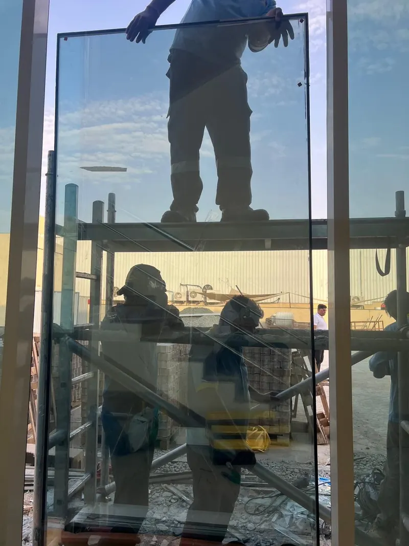 Workers on a mobile scaffold installing curtain wall glazing on a building facade in Dubai Investment Park