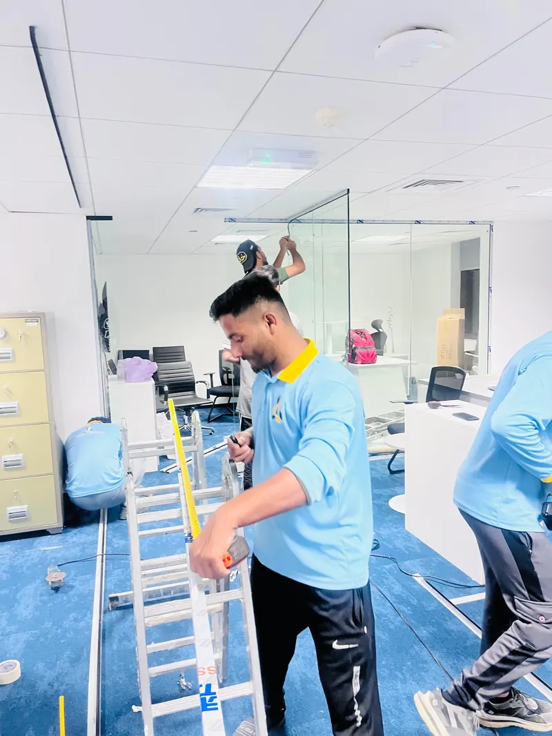 Anas Technical Services worker in company uniform measuring during an office fit-out with glass partitions